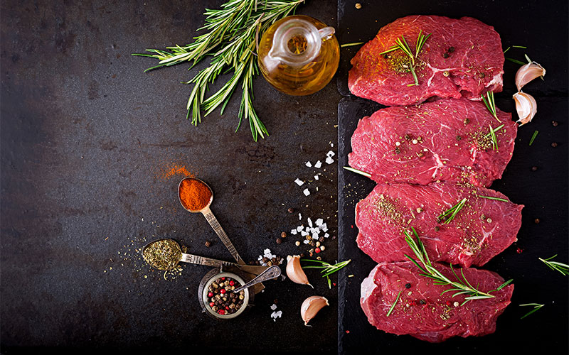 Assortiment de steaks de bœuf premium assaisonnés aux herbes, poivre et ail, prêts pour la grillade à la Boucherie la côte bordelaise.