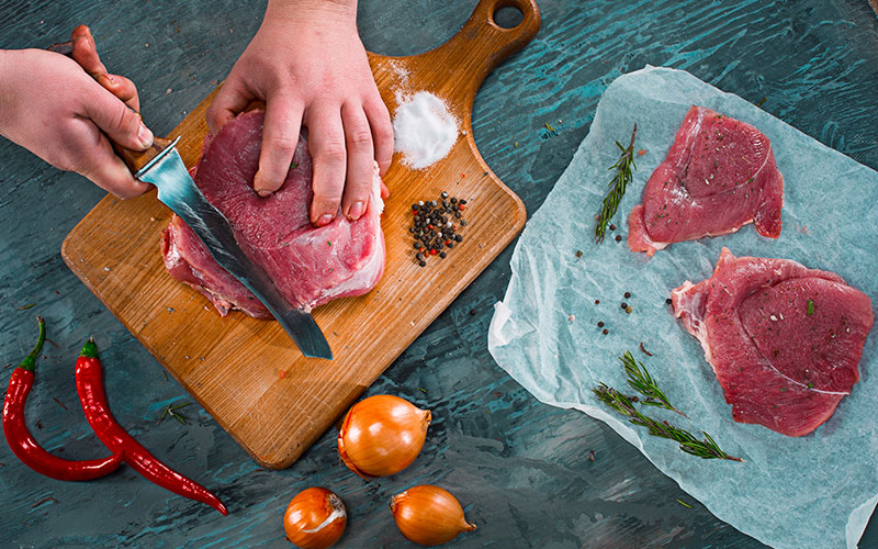 Gros plan d'un artisan boucher découpant avec précision une pièce de viande rouge fraîche avec un couteau professionnel.